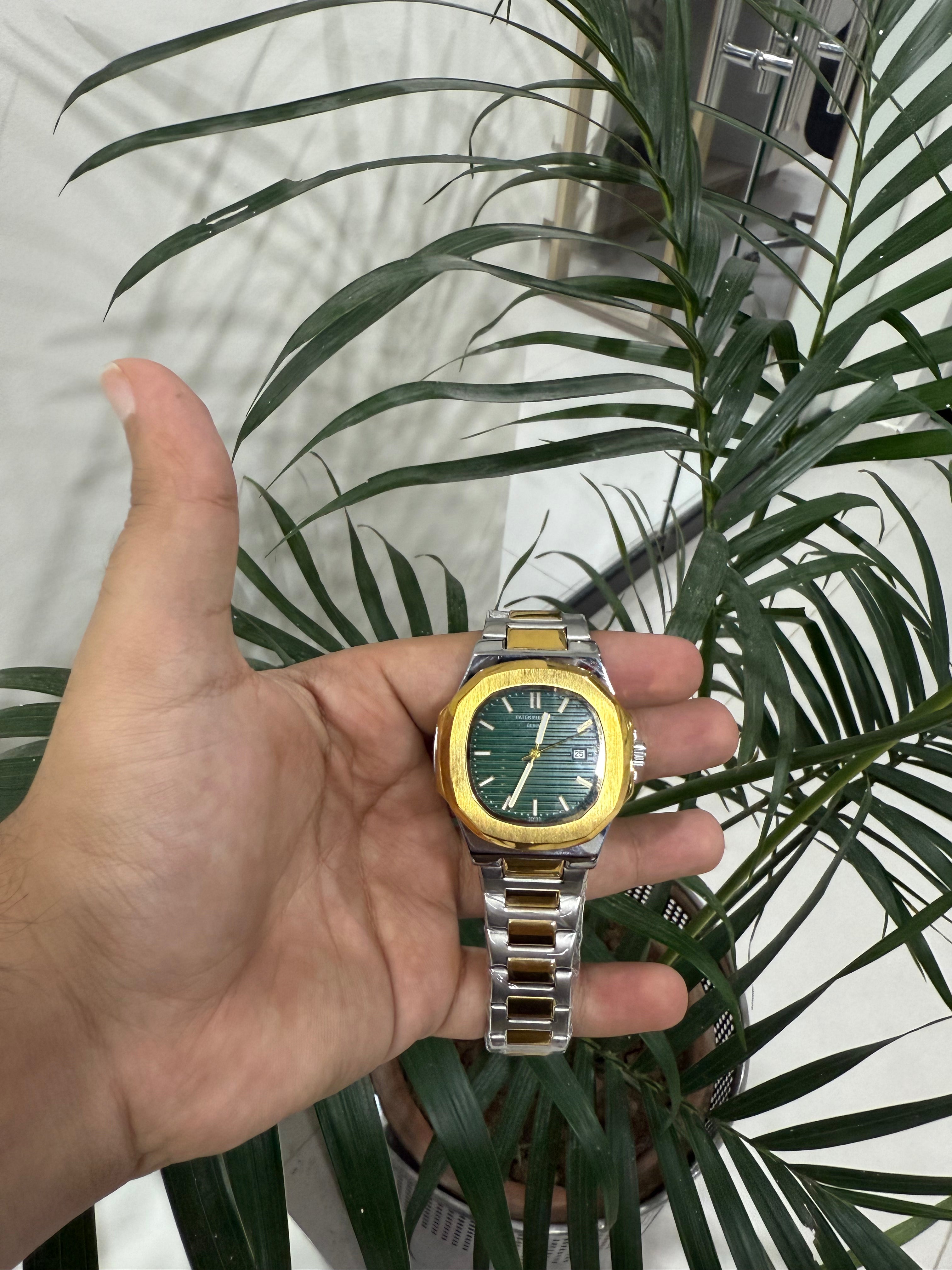 Hand holding  Patek Philippe Nautilus watch with a green dial and gold accents in front of a plant