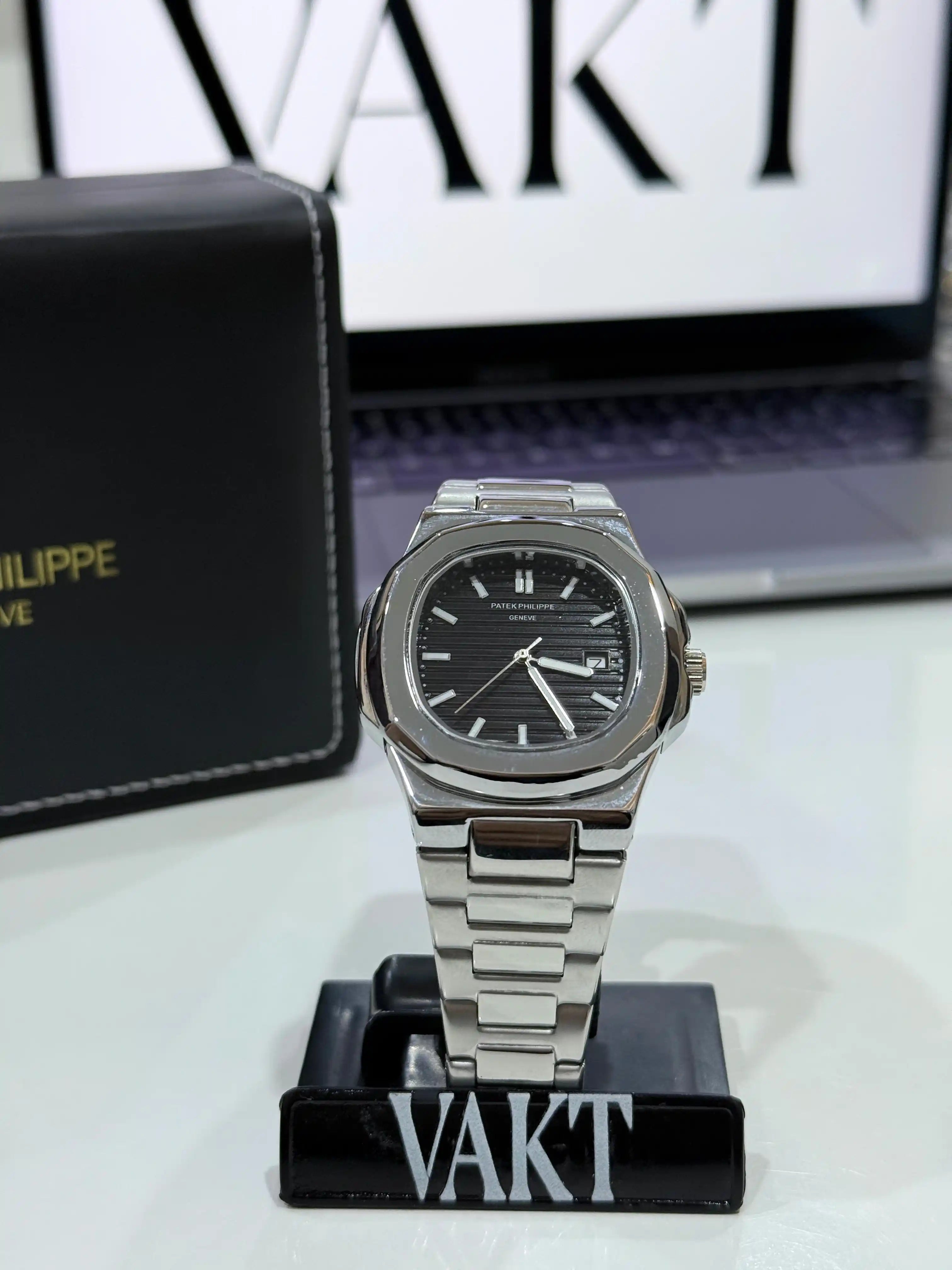 Patek Philippe Nautilus Black Dial Silver watch on a stand with a blurred background featuring a brand name.