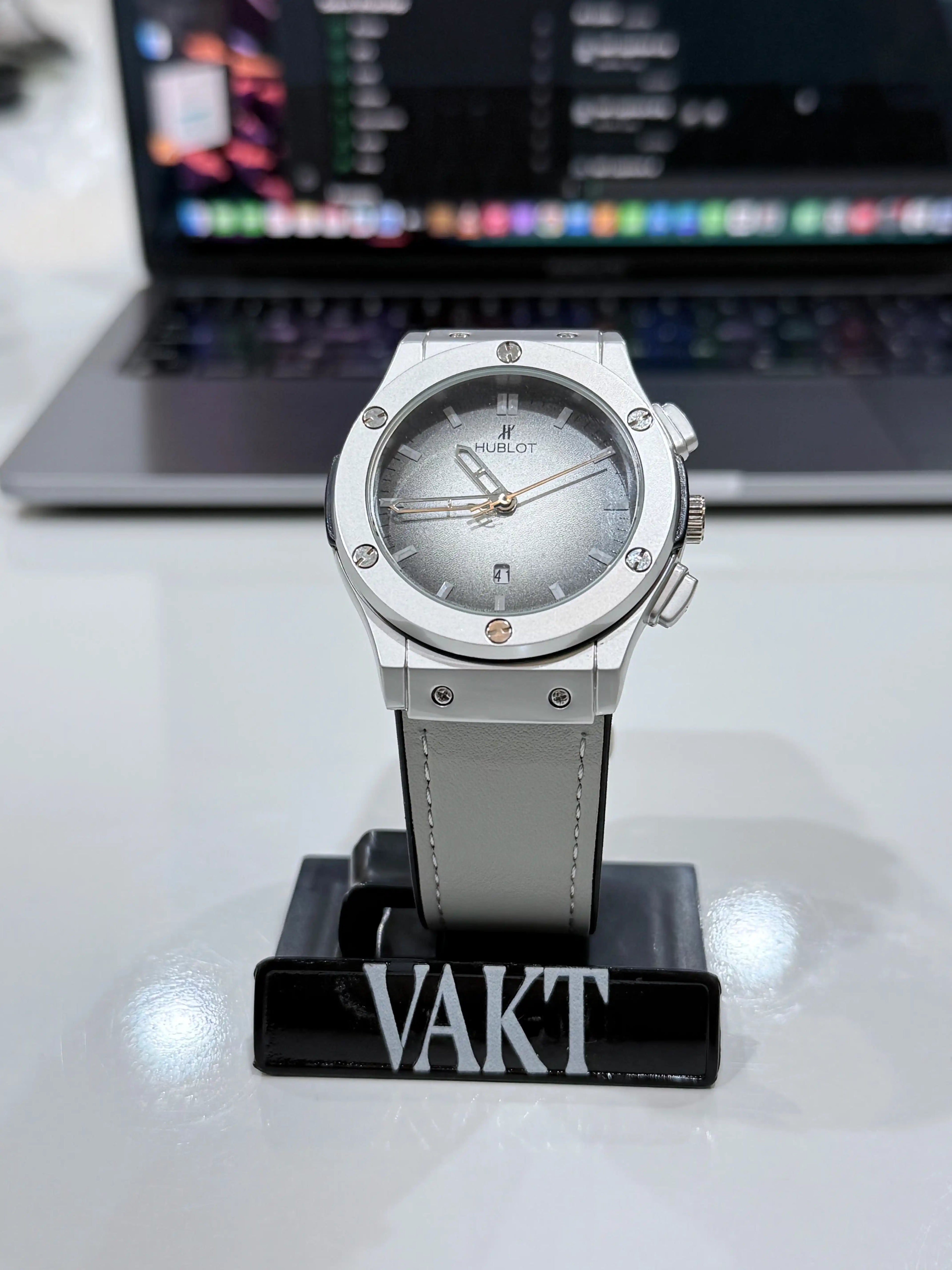 Silver hublot classic fusion watch on a stand with a laptop in the background
