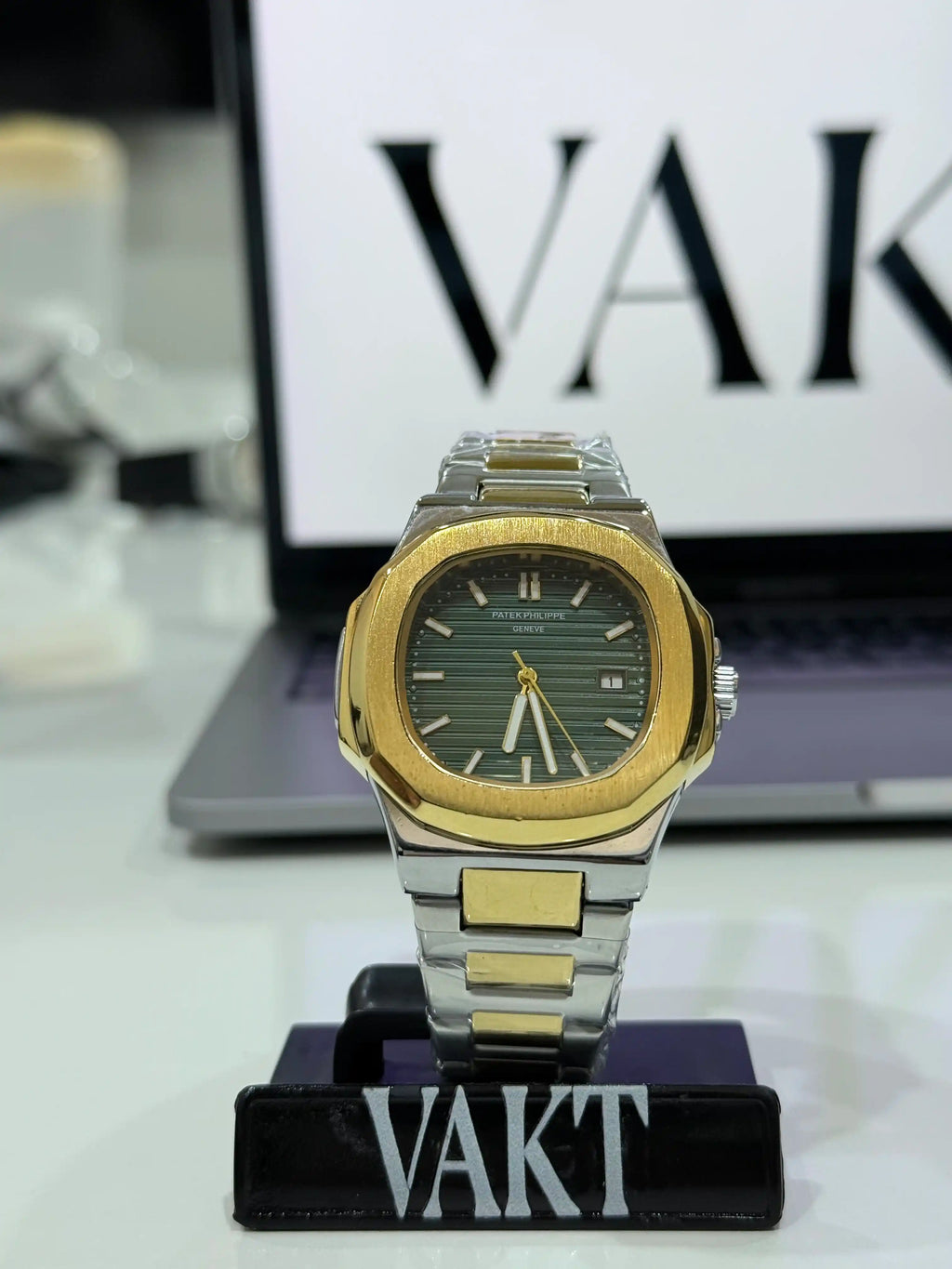 Patek Philippe Nautilus Two-Tone Stainless Steel and Gold Bracelet with Green Dial watch on a stand with 'VAKT' branding in the background