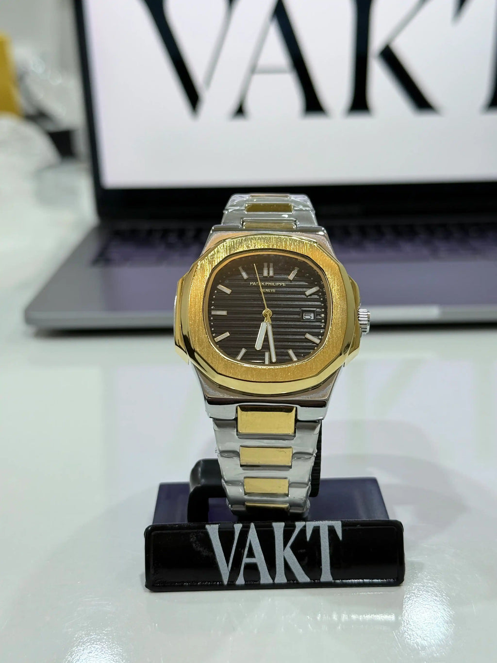Patek Philippe Nautilus Gold and silver watch on a stand with 'VAKT' branding in the background