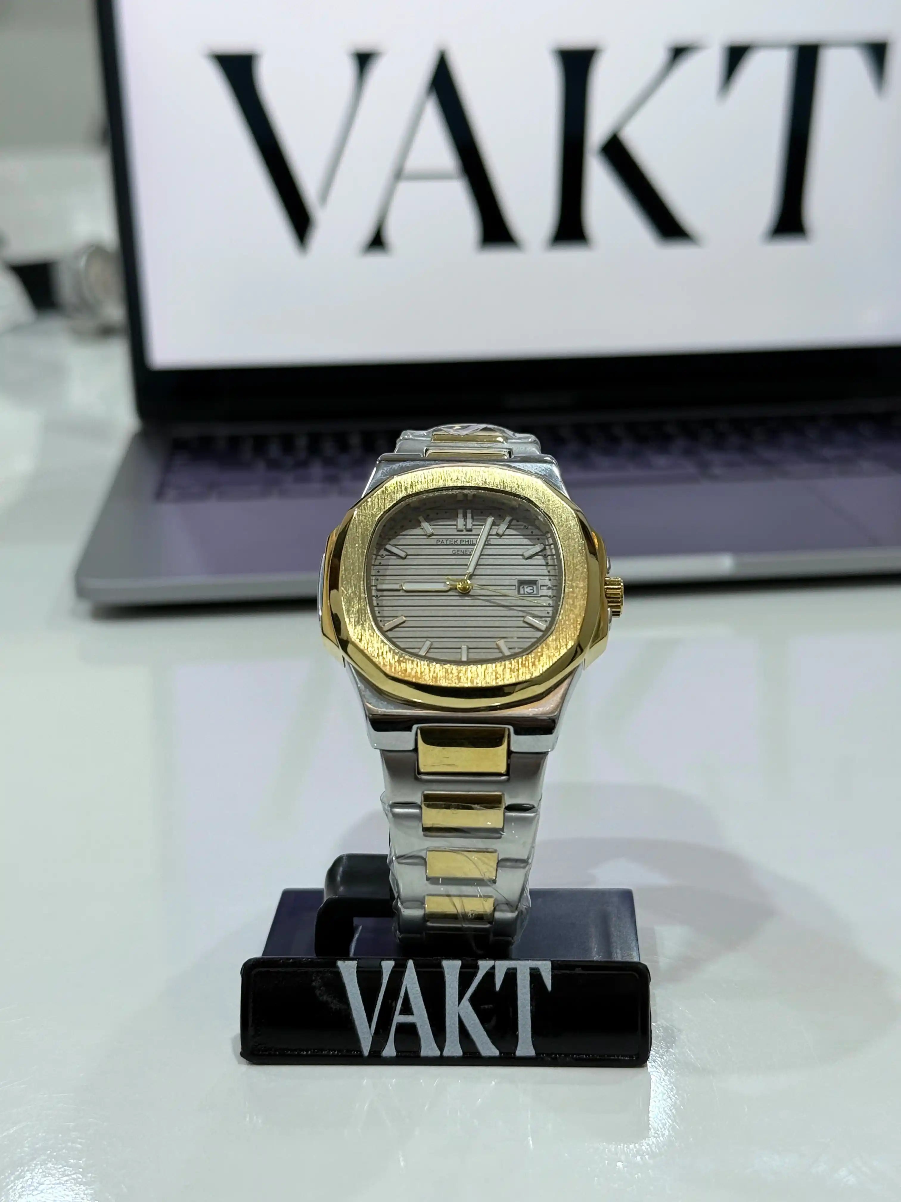 Two-tone Patek Philippe Nautilus watch on a stand with 'VAKT' branding in the background