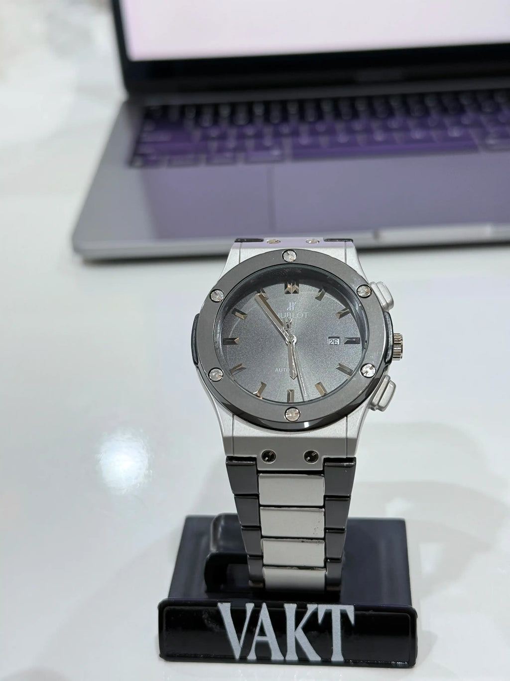 Silver hublot watch on a stand with a laptop in the background