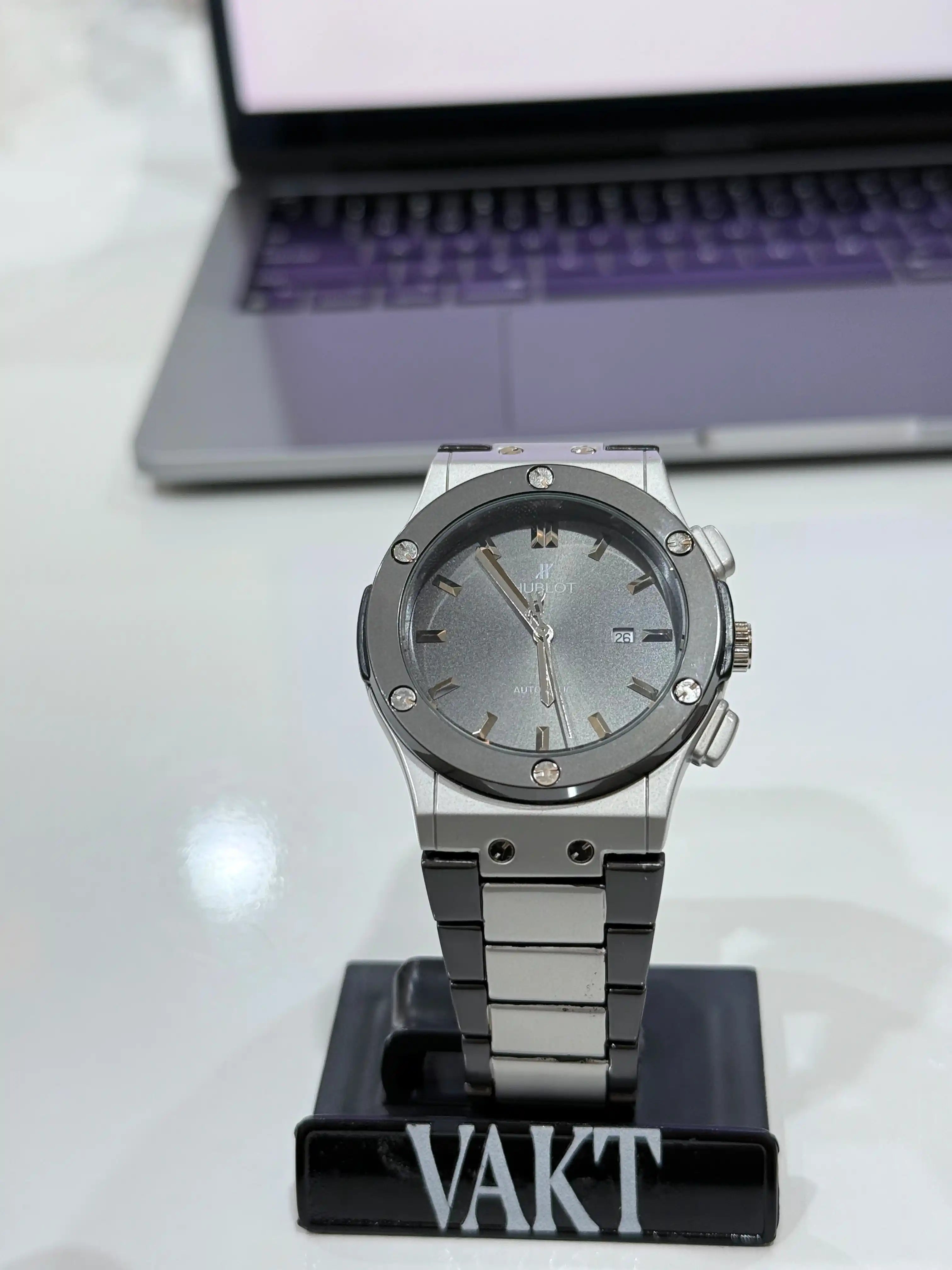 Silver hublot watch on a stand with a laptop in the background