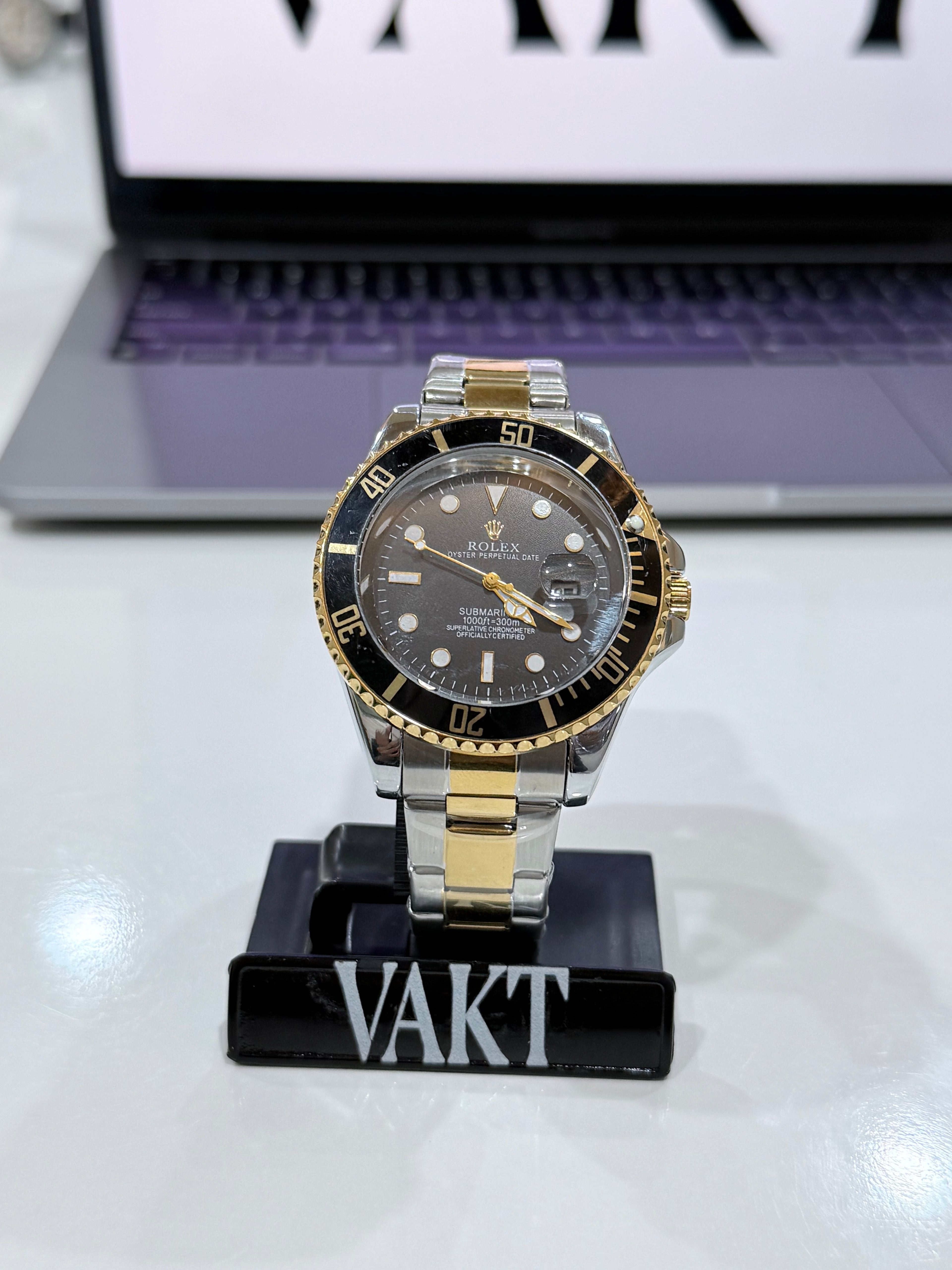 Luxury rolex watch with gold and silver accents on a stand with a laptop in the background