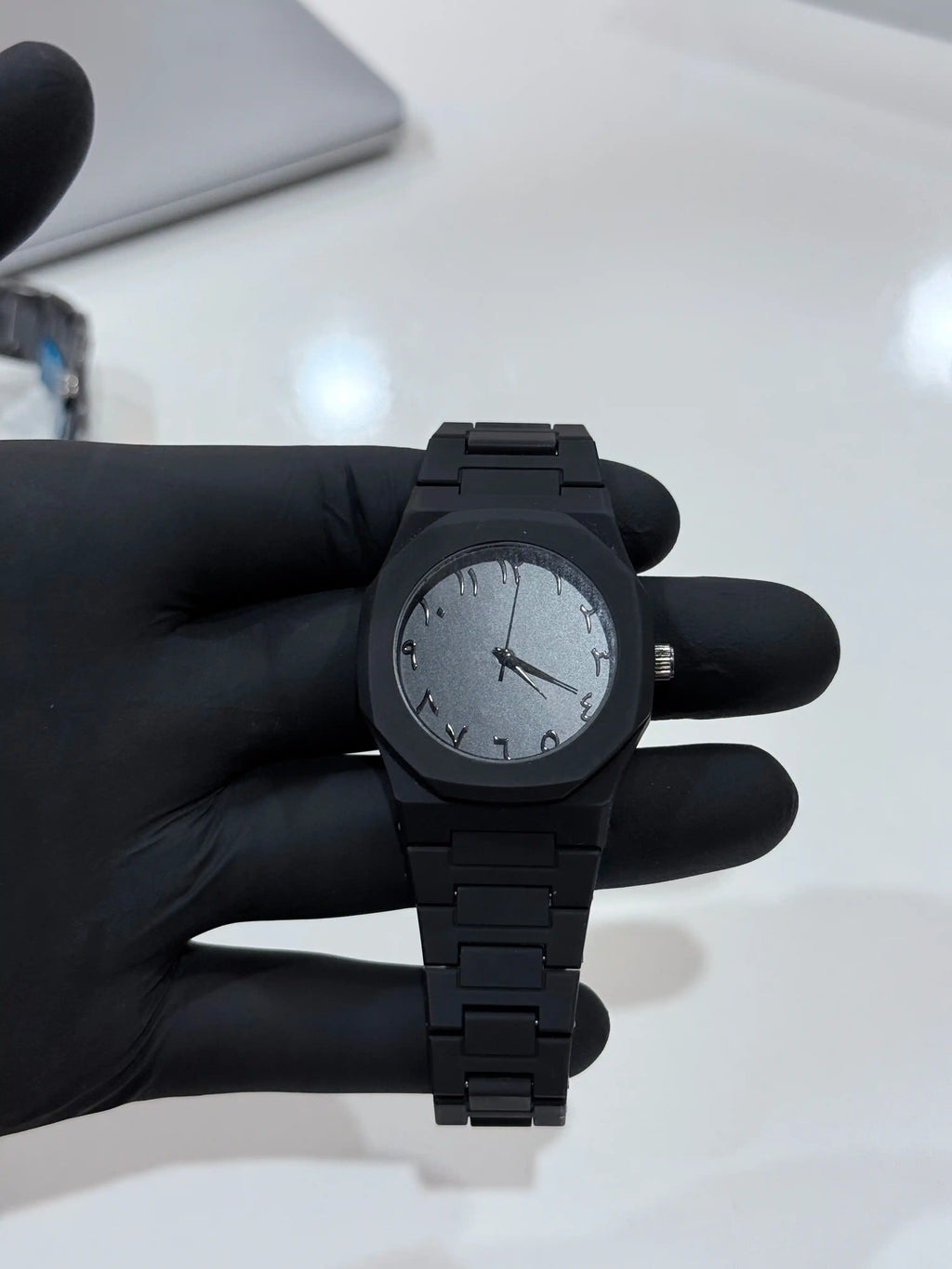 Black arabic aura watch held by a gloved hand on a light background