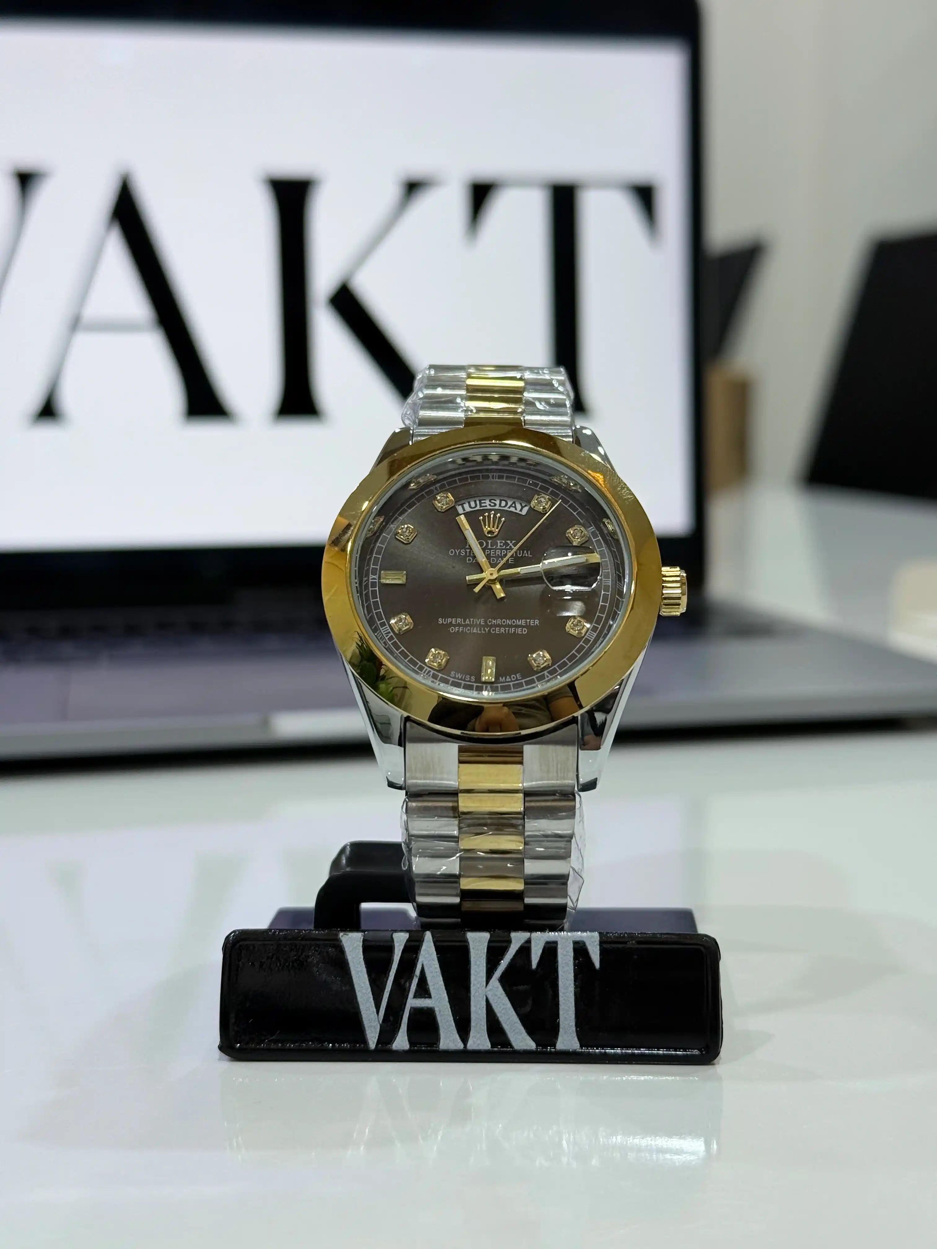 Gold and silver rolex watch on a stand with 'VAKT' branding in the background