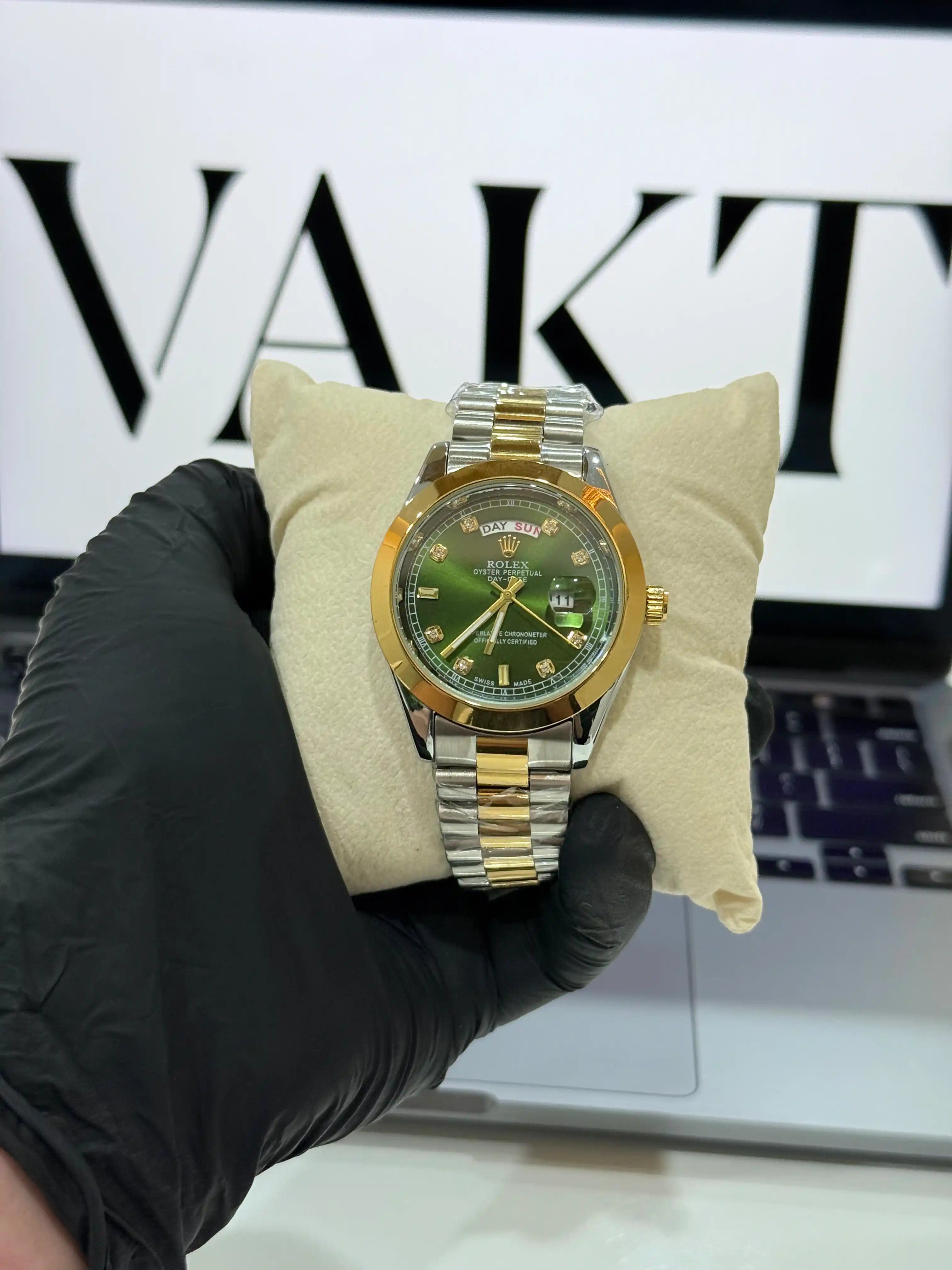 Rolex oyster perpectual day-date Gold and silver watch with green dial held by a gloved hand on a white surface.