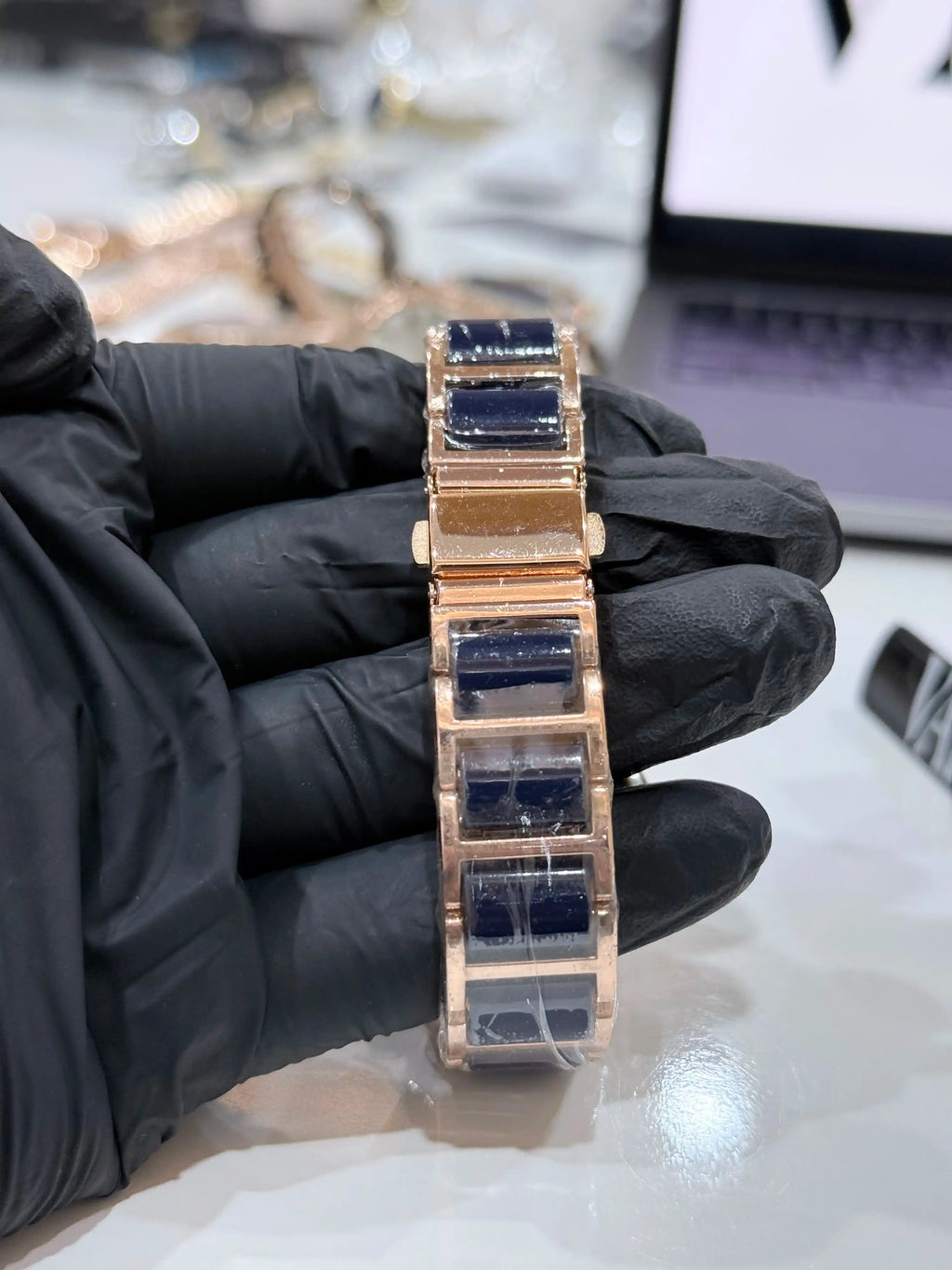 Rose gold watch bracelet with blue stones held by a gloved hand against a blurred background