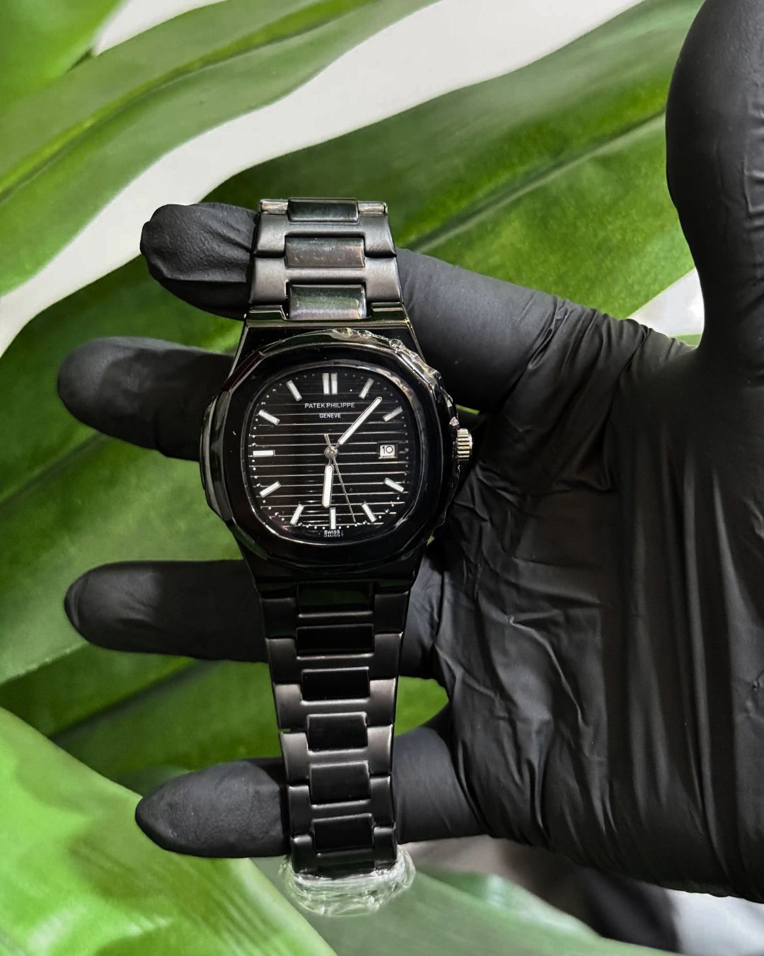 Patek Philippe Nautilus Full Black Stainless Steel watch held by a gloved hand against a green leaf background