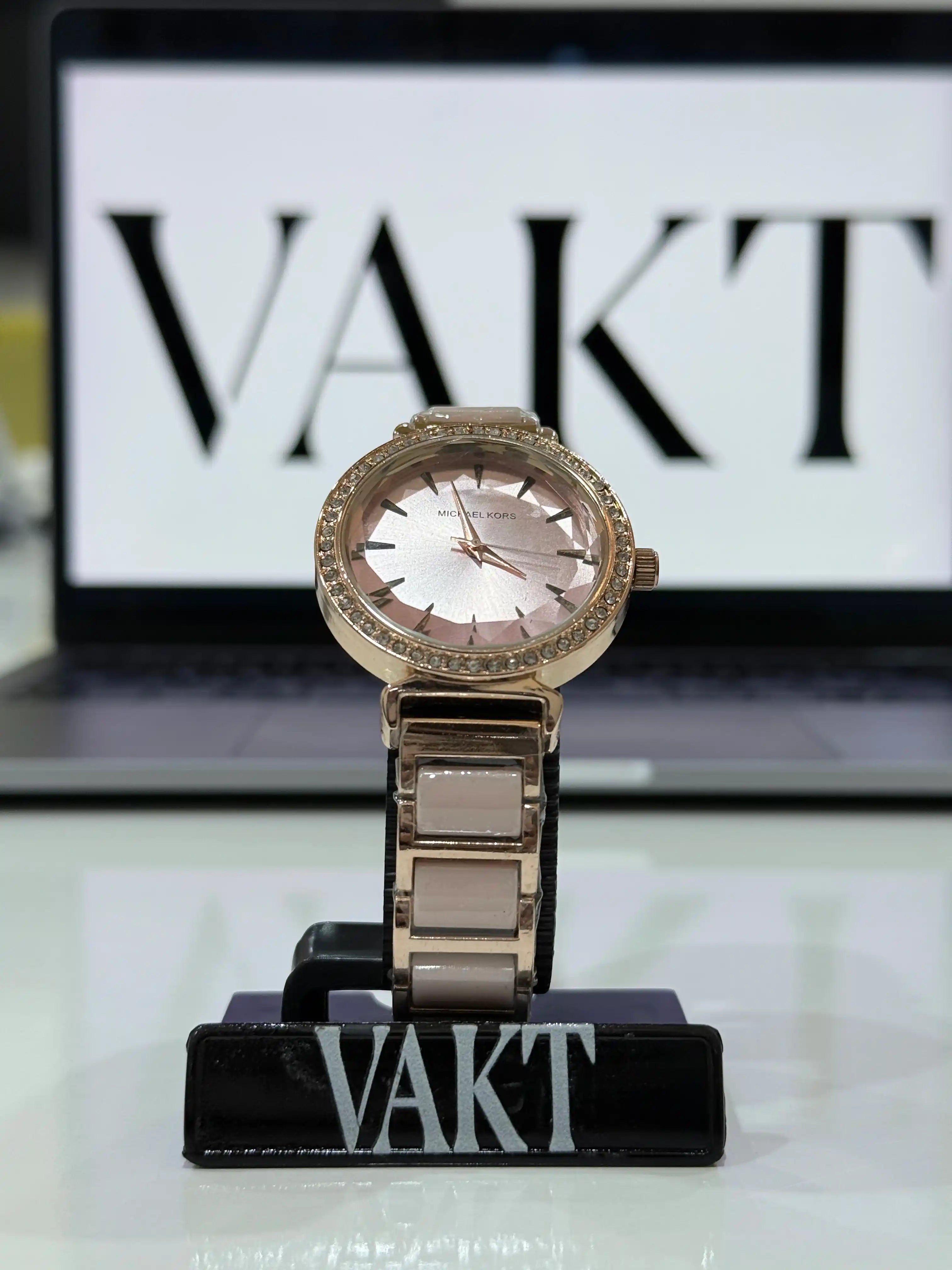 Gold michael kors watch on a stand with 'VAKT' branding in the background