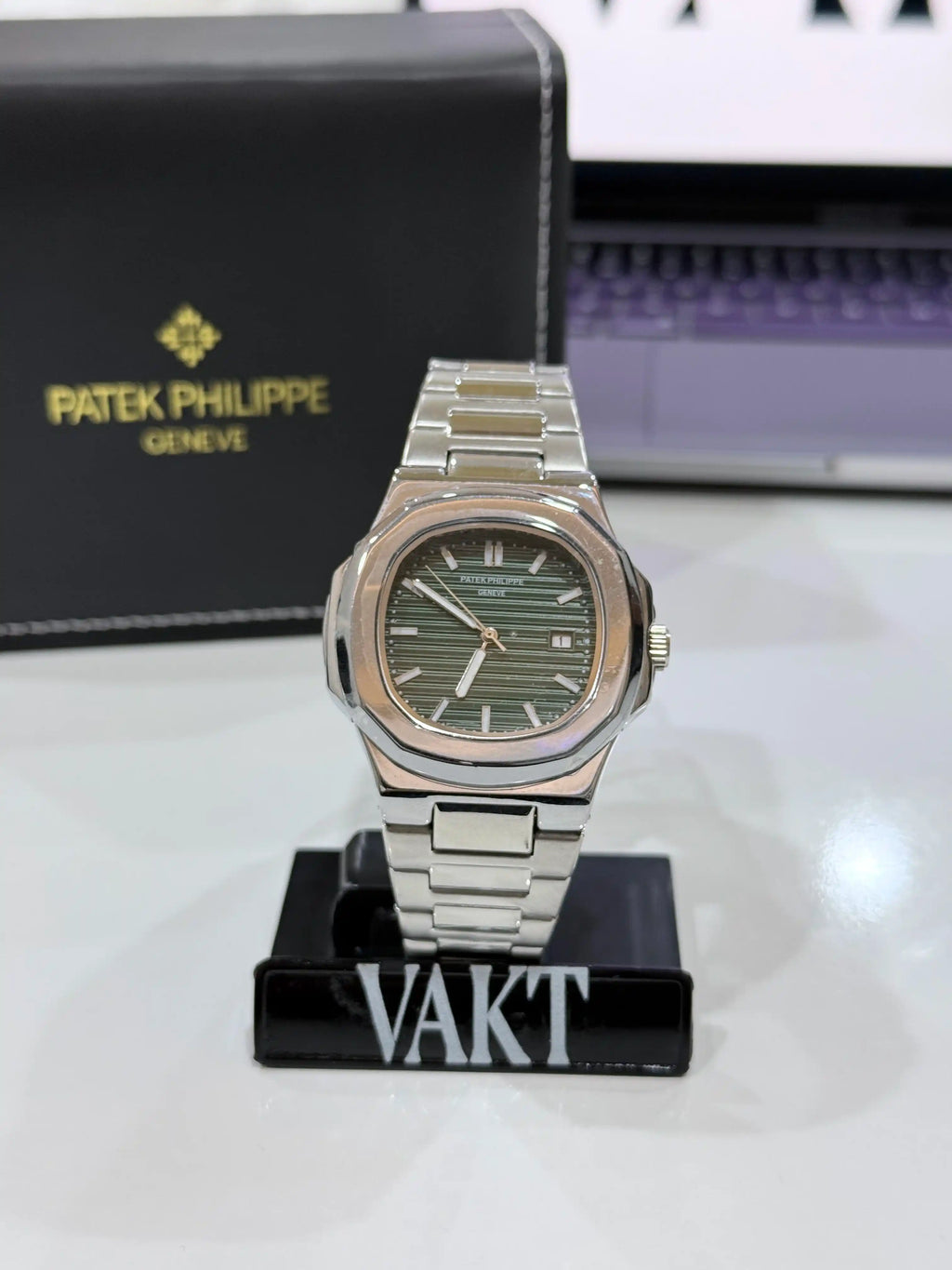 silver patek phillipe watch with a green dial on a stand with a black packaging box in the background