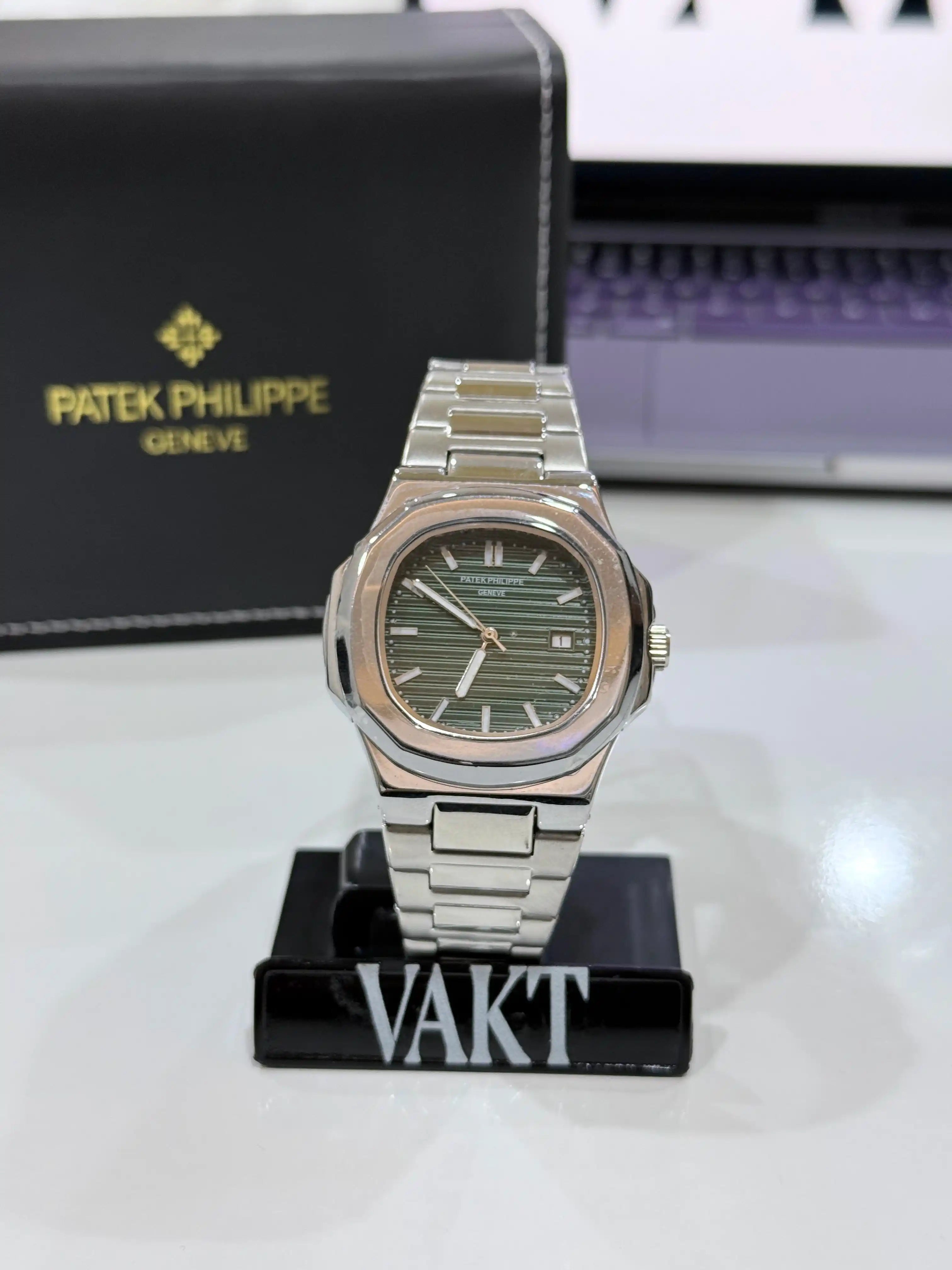 silver patek phillipe watch with a green dial on a stand with a black packaging box in the background