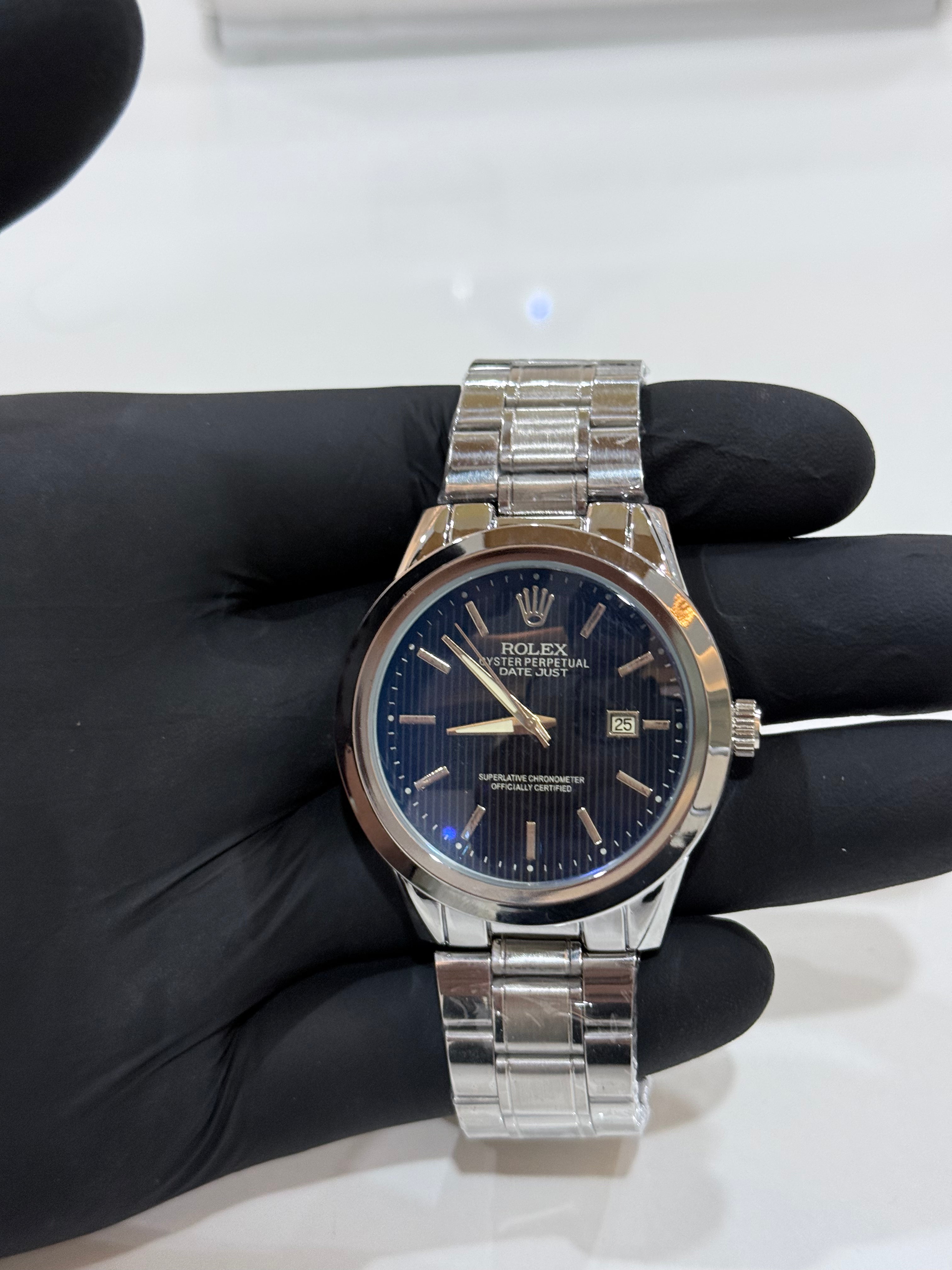 Silver Rolex with a blue dial watch on a black gloved hand against a white background