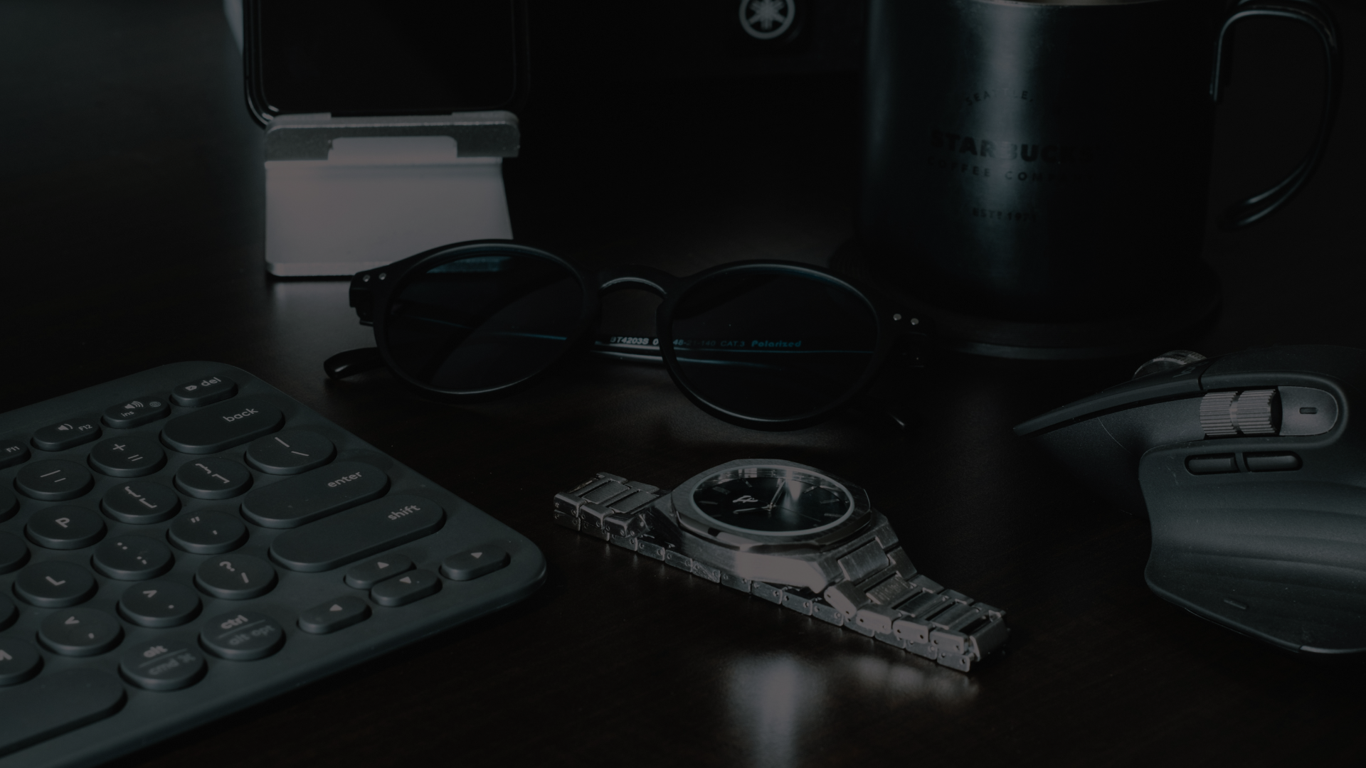 Dark office desk with keyboard, glasses, mug, and mechanical gear