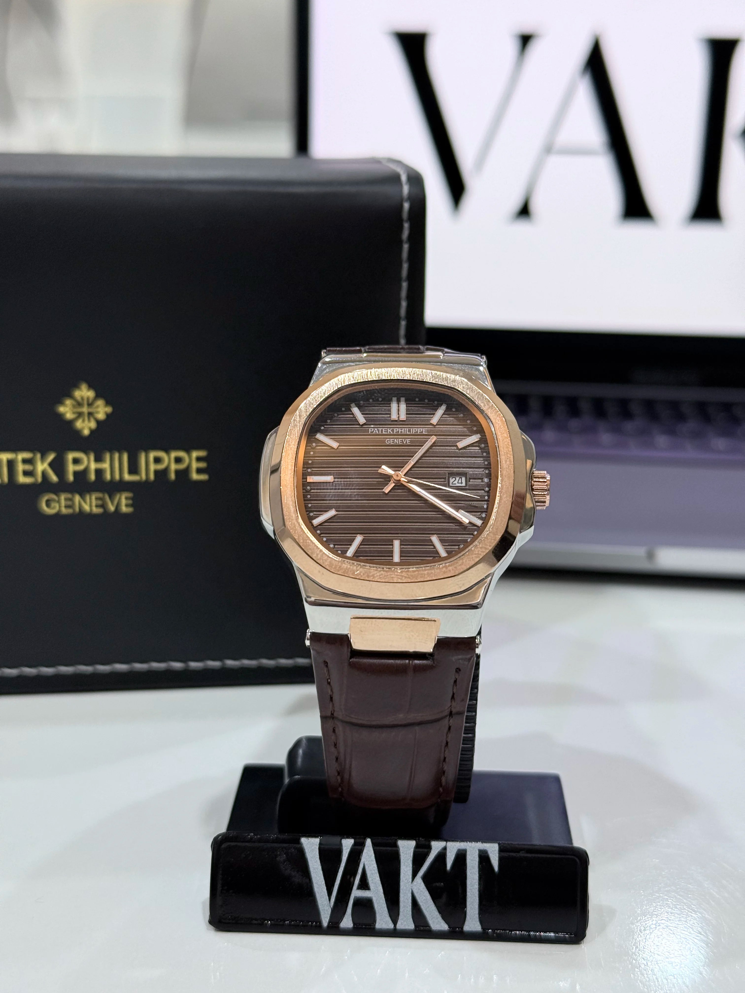 Patek Philippe Nautilus watch in rose gold with a brown dial and a brown leather strap on a stand with 'Vakt' branding in the background